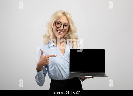 Happy female entrepreneur pointing at laptop computer with blank screen for website design on light studio background Stock Photo