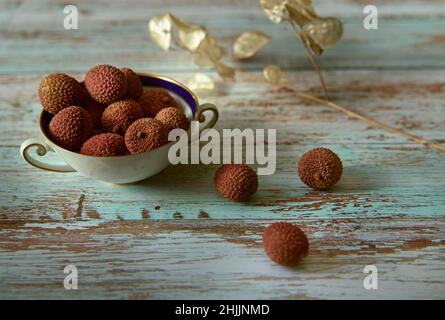 Litchi or Chinese plum in a white ceramic bowl on a wooden table. Stock Photo