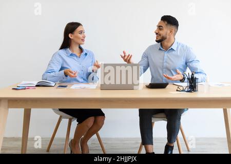 Portrait Of Smiling Colleagues Talking Sitting At Desk Stock Photo