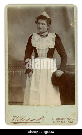 Original Victorian Carte de Visite (CDV) or visiting card of attractive maid, parlour maid, in uniform, wearing a white apron with bib and a lace cap, F.G. Simpson & Co. 17 Wharf Road, Grantham, Lincolnshire, U.K. circa 1888 Stock Photo