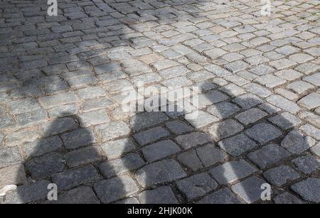 Shadows of three people on the cobblestone pavement