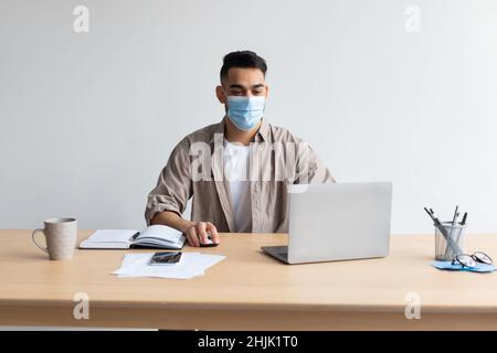 Man in disposable facemask working on pc at home office Stock Photo