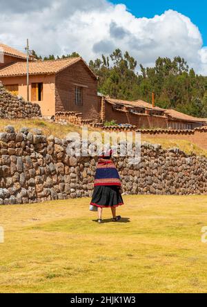 Peruvian indigenous quechua woman in traditional clothing walking in front of an inca wall of the Chinchero inca ruin, Peru. Stock Photo