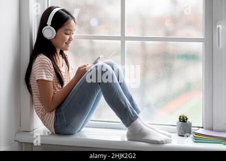 Joyful korean girl schooler playing games on cellphone, using headset Stock Photo