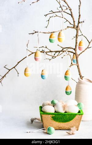 Painted Easter egg decorations hanging on branches next to a box of Easter eggs Stock Photo