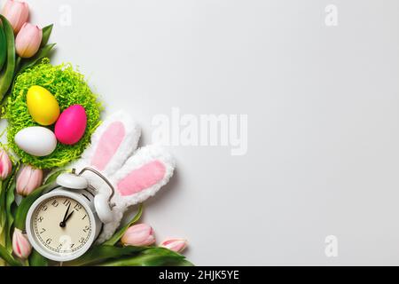 Easter card. Multi-colored eggs in nests flowers tulips alarm clock with rabbit ears on a gray background. copy space Stock Photo