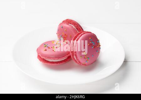 Three pink macarons with creamy fillings and sprinkles on plate Stock Photo