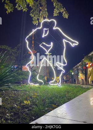 Vertical shot of a neon sign in the shape of dancing couple glowing on city street Stock Photo