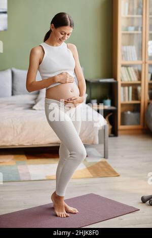 Young pretty woman touching her pregnant belly and enjoying her pregnancy while standing in the bedroom at home Stock Photo