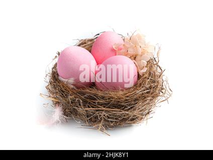 Three pink eggs in a nest decorated with flowers on a white background. Side view, close-up. The concept of Easter. Stock Photo