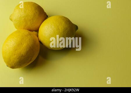 three organic lemons from sicily (siracusa) on a light yellow paper background with plenty of room for text Stock Photo