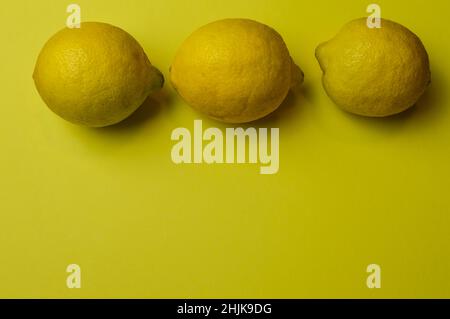 three organic lemons from sicily (siracusa) on a light yellow paper background with plenty of room for text Stock Photo