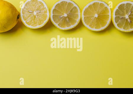 arrangement of four half lemons lined up with one whole lemon on a light yellow paper background and plenty of room to add text Stock Photo
