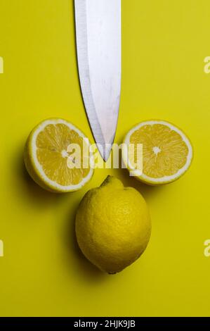 arrangement of two half lemons and one whole lemon with a knife blade on a light yellow paper background Stock Photo