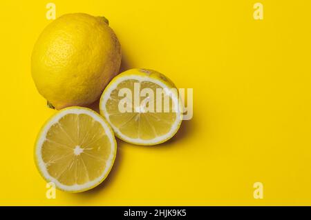two half lemons and one whole lemon on a yellow paper background with plenty of room for text Stock Photo
