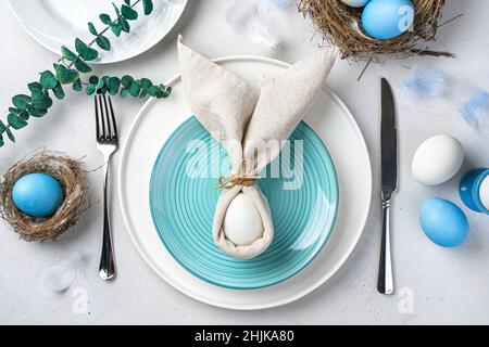 Festive Easter table setting with Easter bunny made of linen napkin and egg. Top view. Stock Photo