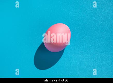 Pink egg on a blue background with a hard shadow. The concept of Easter, minimalistic food. Stock Photo