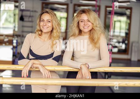 Portrait of cheerful sporty young women smiling at camera while leaning on ballet barre after exercising in modern pilates studio. Healthy lifestyle, sports concept Stock Photo