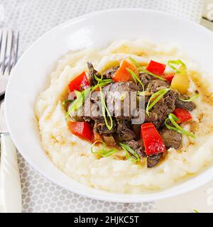 Fried chicken liver with apples, sweet pepper and onions with mashed potatoes  a bowl on white wooden table. Stock Photo