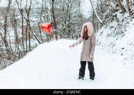 Girl standing on the road in the forest holding one red helium balloon Stock Photo