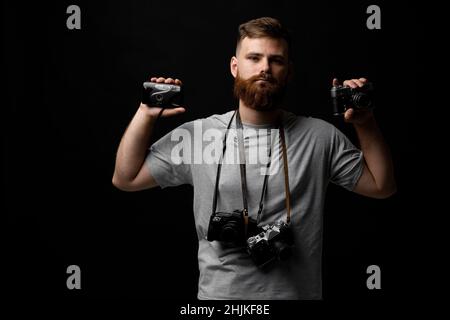 Professional handsome bearded male photographer with bunch of vintage photo cameras in photo studio, isolated on black background. Stock Photo