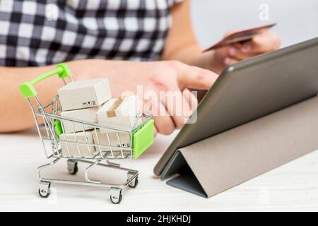 Paper boxes in trolley, womans hands holding credit card and using tablet to shop online. Online shopping concept Stock Photo