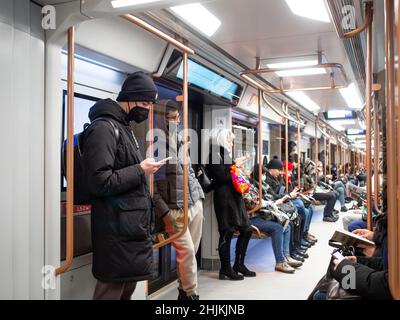 Moscow. Russia. January 26, 2022. A young man in a protective mask holds a smartphone in his hands while standing in a subway car. Selective focus.