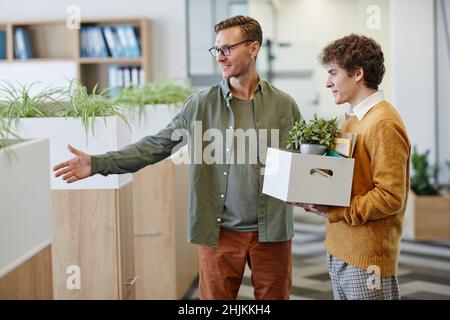 Portrait of smiling male manager welcoming new employee in office and showing workplace, copy space Stock Photo
