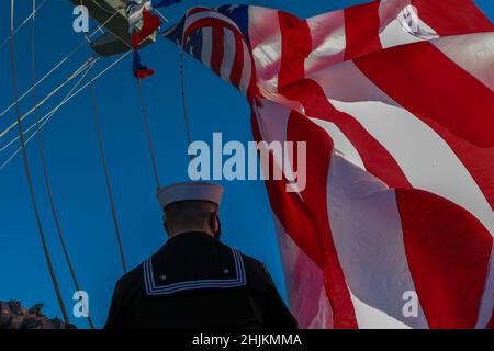 SAN DIEGO (Jan. 3, 2022) Quartermaster 2nd Class Steven Pettit, from Ionia, Mich., hoists the ensign on the mast aboard USS Abraham Lincoln (CVN 72). The Abraham Lincoln Carrier Strike Group, led by Carrier Strike Group 3, deployed from San Diego, Jan. 3, in support of global maritime security operations. An integral part of U.S. Pacific Fleet, U.S. 3rd Fleet operates naval forces in the Indo-Pacific and provides the realistic, relevant training necessary to flawlessly execute our Navy’s role across the full spectrum of military operations — from combat operations to humanitarian assistance an Stock Photo