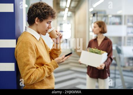 Side view portrait of young employees on break in office focus on man drinking coffee in background, copy space Stock Photo