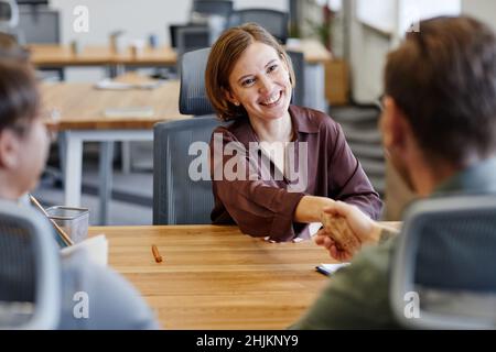 Portrait of smiling young woman shaking hands with HR manager at job interview in office, copy space Stock Photo