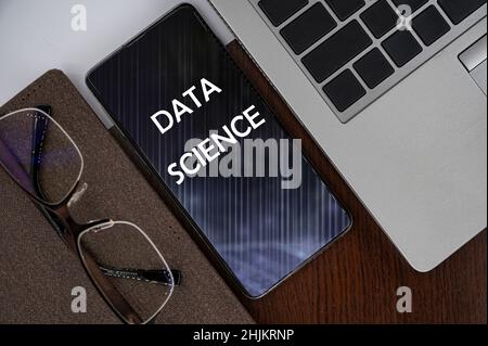 Top view of phone on table near laptop, notepad and glasses with inscription data science. Learn data science, computer courses, training. Stock Photo