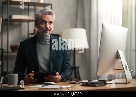 Mature businessman indoors in office, working on tablet. Stock Photo