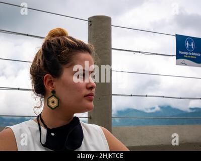 Guatape, Antioquia, Colombia - December 8 2021: Colombian Woman with Dyed Hair and Big Earrings has Black Mask on her Neck Stock Photo