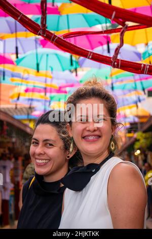 Guatape, Antioquia, Colombia - December 8 2021: Women Friends Pose and Look at the Camera in the Street of Colorful Umbrellas Stock Photo