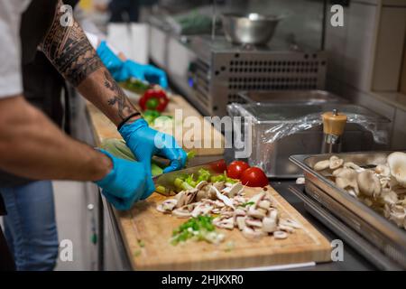 Unrecognizable chef with gloves cutting vegetables indoors in restaurant kitchen. Stock Photo