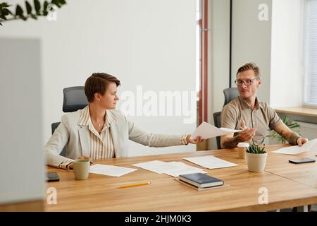 Portrait of two business people reviewing documents while sitting at desk in modern office Stock Photo