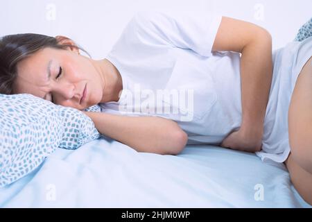 Young woman lying in the bed and suffering from gynecological problems, menstruation pain, stomach ache or abdominal pain. Menstruation period or PMS Stock Photo