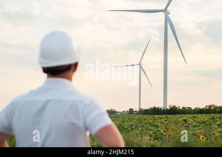 An engineer in a white helmet  is looking at the wind turbines. A man in a helmet supervises the operation of the electric windmills. Ecology and rene Stock Photo