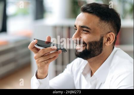 Phone call concept. Positive handsome successful Indian man, information technology specialist, top manager, department manager, talking on a mobile phone with clients or colleagues on speakerphone Stock Photo