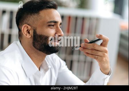 Close-up portrait of handsome successful confident Indian business man, IT specialist, manager, director,recording work voice message on mobile phone for colleague or client or talking on speakerphone Stock Photo