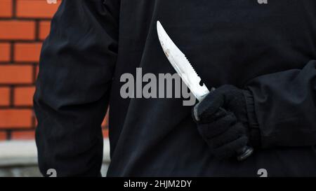 Man with the knife behind his back. Man holding sharp knife behind his back. Stock Photo
