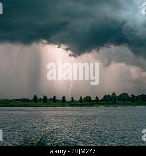 Positive cloud to ground lightning discharge near a lake at dusk Stock Photo