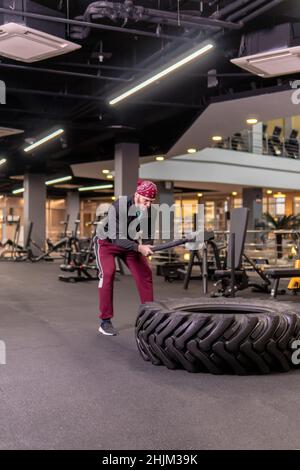 A man hits a sledgehammer wheel in fitness, the concept of a healthy lifestyle male sledgehammer active hit sport, from strength muscular in adult and Stock Photo