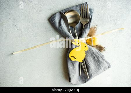 Minimalistic table setting with grey napkin and cutlery decorated with wooden bunny Stock Photo