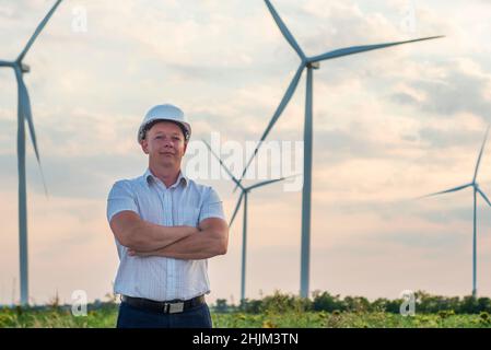 A man in a helmet is standing on windmills background. Architect or engineer standing in front of windmills. Stock Photo