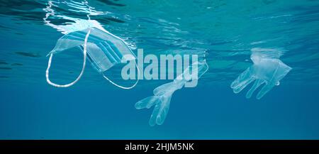 Ocean pollution Coronavirus waste, plastic face mask and gloves underwater below water surface, COVID-19 pandemic Stock Photo
