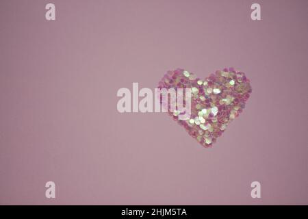 Pink heart made of sequins on a red table. Copy space Stock Photo