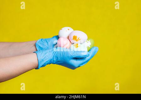 Hands in blue medical gloves holding painted easter eggs. Easter time in quarantine concept. Concept of Easter holyday during epidemy of coronavirus. Stock Photo