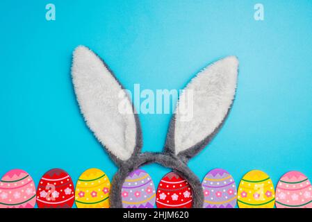 Colorful painted Easter eggs with bunny ears on blue background. Top view. Easter greeting card. Stock Photo